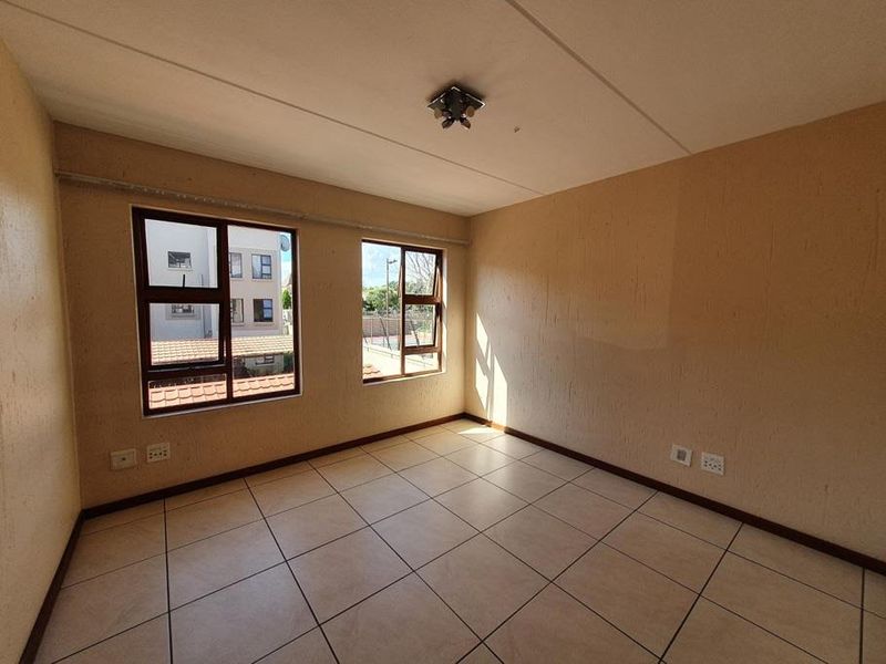 An empty bedroom featuring neutral textured walls, tiled flooring, and large aluminium-framed windows providing natural light.