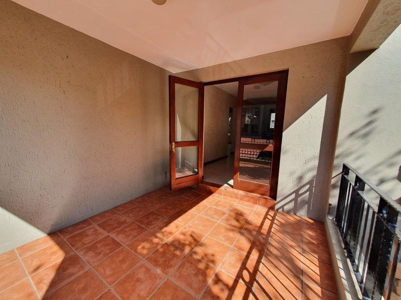A covered balcony featuring terracotta floor tiles, a metal balustrade, and double glass doors providing access to the interior living space.
