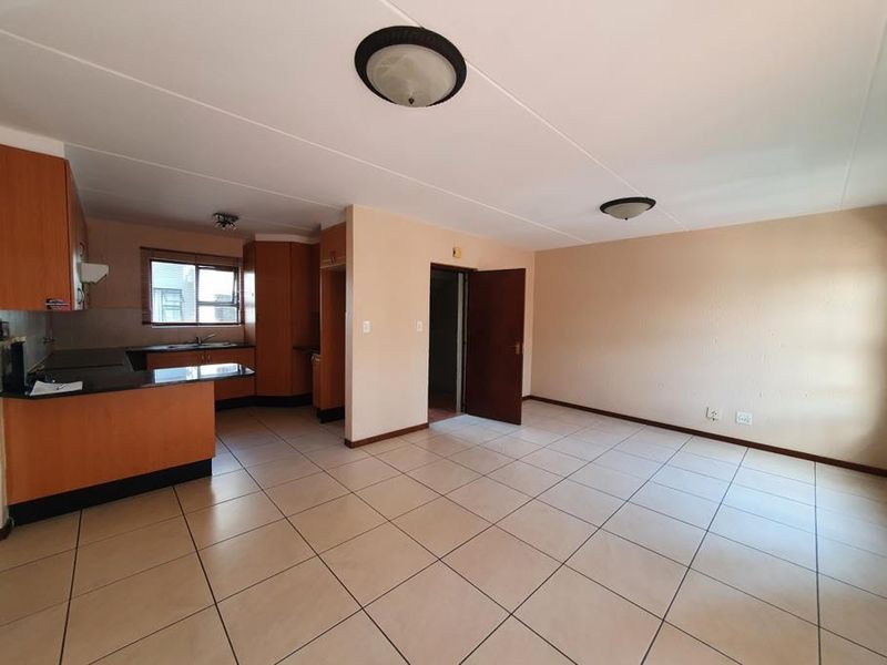 An open-plan living and kitchen area featuring tiled flooring, built-in wooden cabinetry, and neutral wall finishes in a vacant apartment setting.