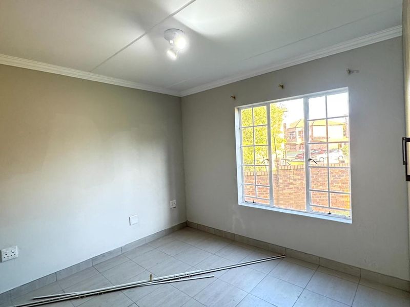 An empty bedroom featuring tiled flooring, a multi-pane window, and a built-in cupboard, providing a neutral canvas for personalization.