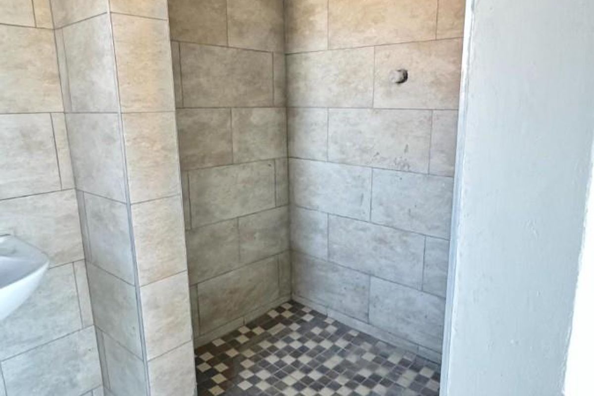 A tiled walk-in shower area featuring a shower head and mosaic floor tiling, currently missing a mixer handle.