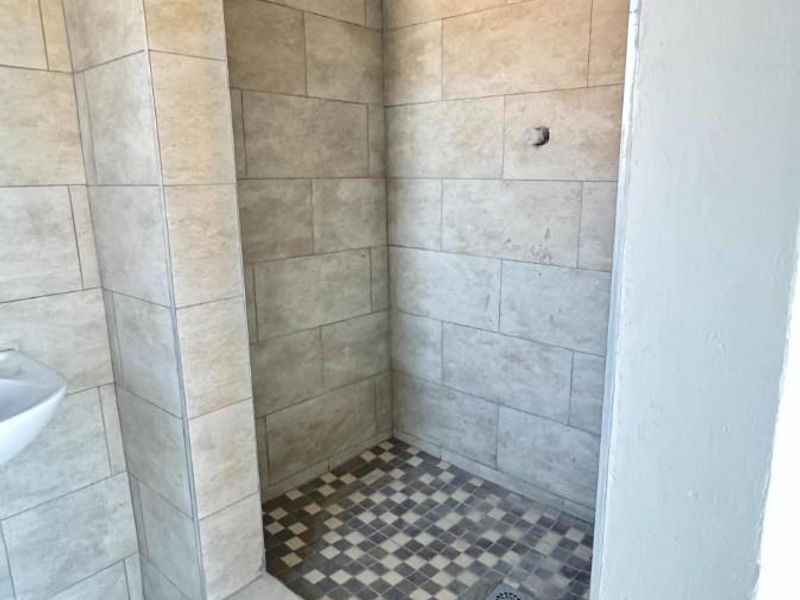 A tiled walk-in shower area featuring a shower head and mosaic floor tiling, currently missing a mixer handle.