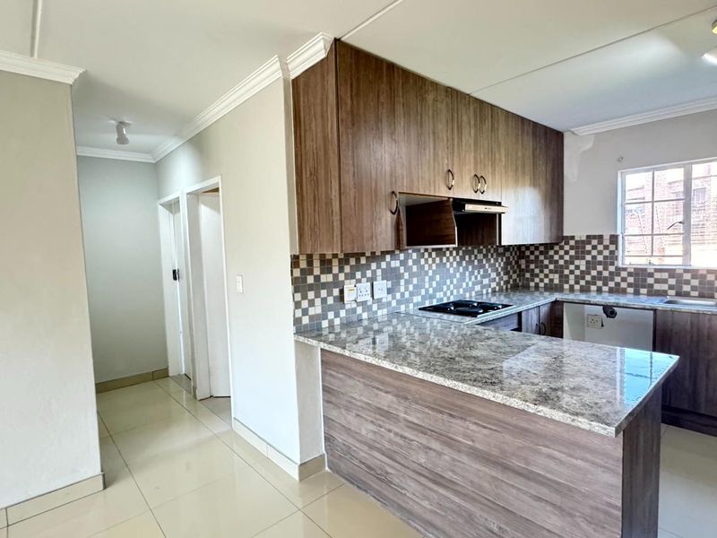 Modern kitchen featuring granite countertops, wood-finish cabinetry, built-in hob, extractor fan, and tiled backsplash, offering a functional and clean workspace.