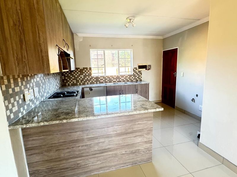 A functional kitchen featuring granite countertops, wood-finish cabinetry, a built-in hob, and tiled flooring, offering a clean and practical workspace.
