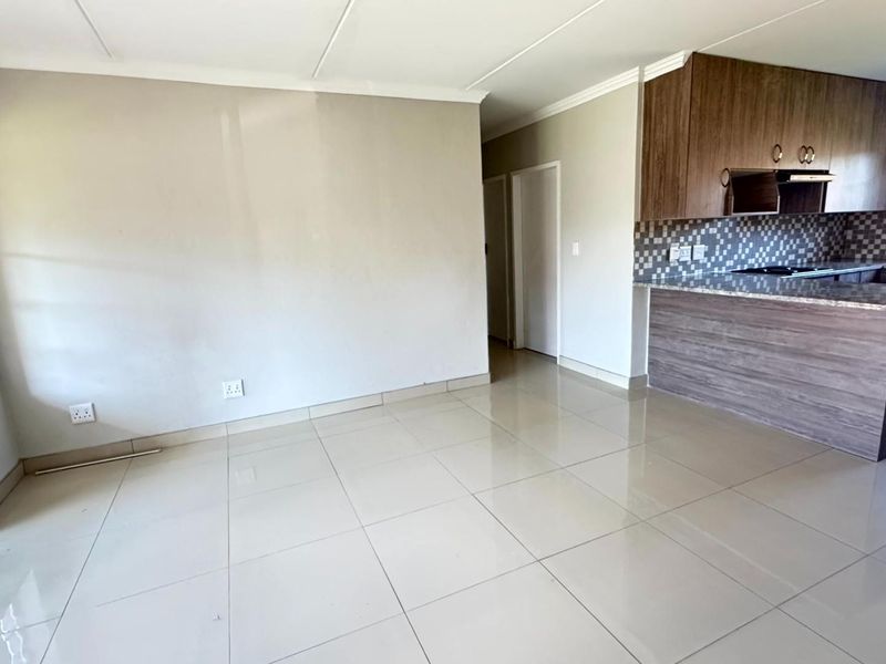 An open-plan living and kitchen area featuring tiled floors, modern wood-finish cabinetry, granite countertops, and a security gate on the window.