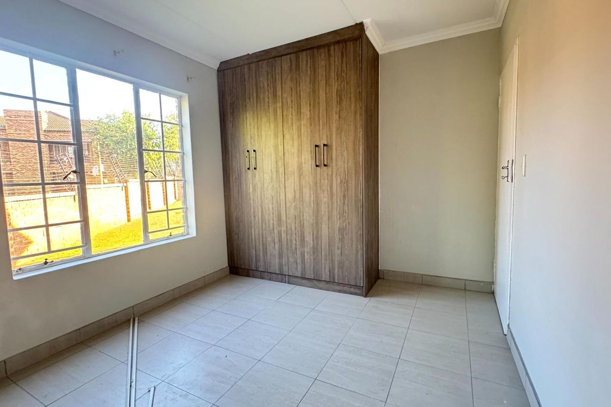 A bright, empty bedroom featuring tiled flooring, neutral walls, and a large built-in wooden wardrobe.