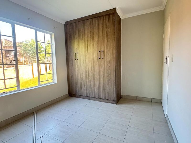 A bright, empty bedroom featuring tiled flooring, neutral walls, and a large built-in wooden wardrobe.