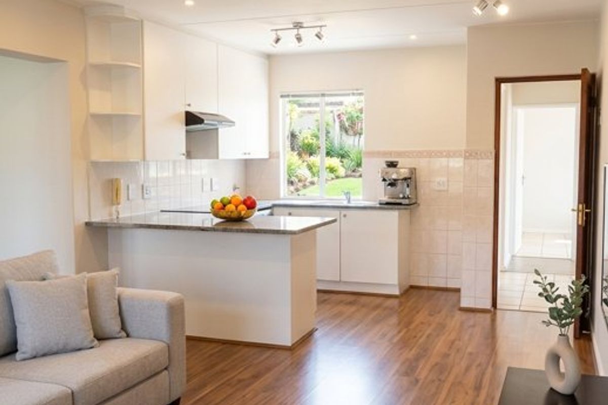 A bright open-plan living and kitchen area featuring modern laminate flooring, granite countertops, and clean white cabinetry with integrated lighting.