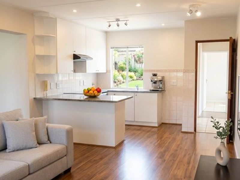 A bright open-plan living and kitchen area featuring modern laminate flooring, granite countertops, and clean white cabinetry with integrated lighting.