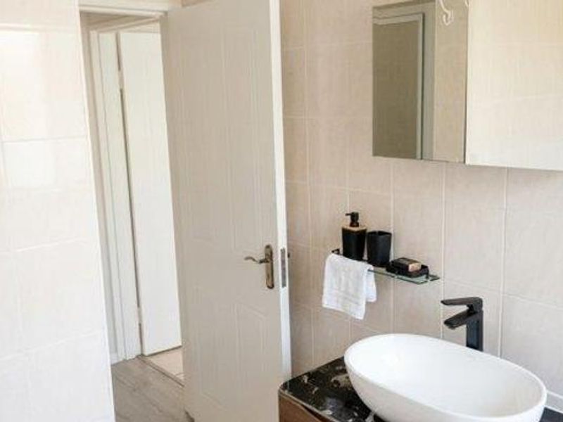 A modern bathroom featuring a vessel sink with a black mixer tap, a vanity cabinet, and a mirrored medicine cabinet against tiled walls.