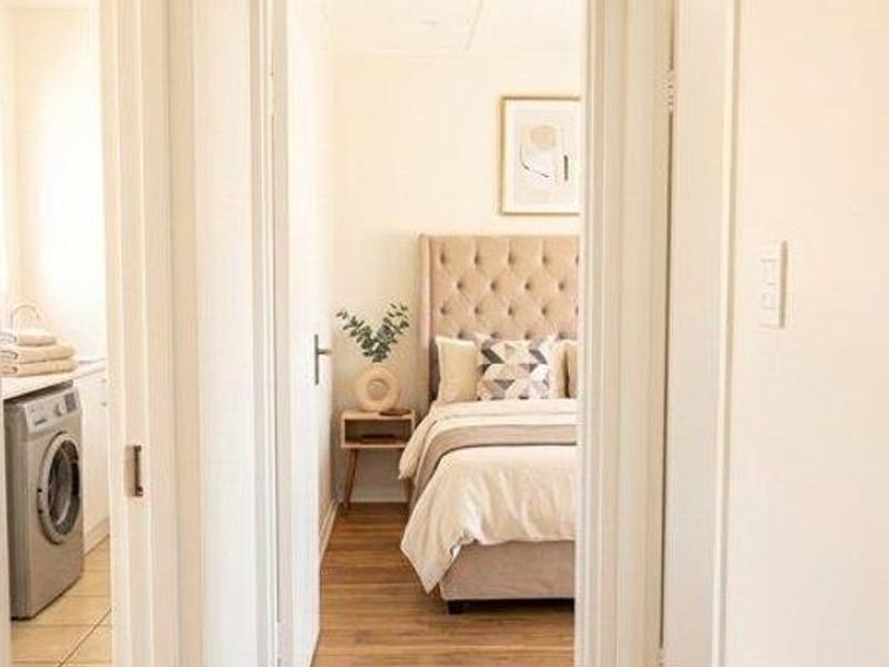 A view through a hallway connecting a laundry area to a bedroom, featuring neutral tones and laminate flooring.