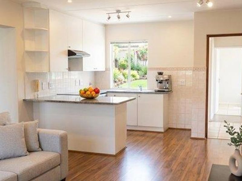 Open-plan kitchen featuring granite countertops, white cabinetry, and laminate flooring, seamlessly connecting to the living area with views of the garden.