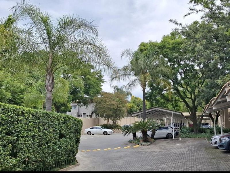 A view of the apartment complex exterior featuring a paved driveway, covered parking bays, and established garden landscaping.