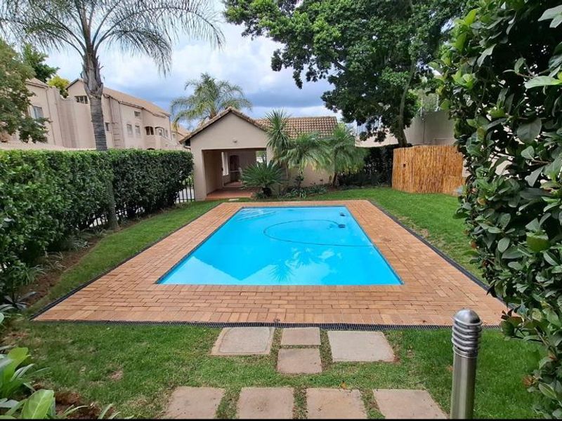 A well-maintained private swimming pool area featuring brick coping, lush surrounding garden, and established hedging in a residential apartment complex setting.