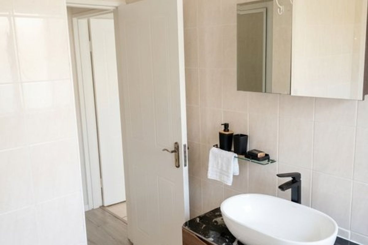 A modern bathroom featuring a dark marble-topped vanity with a vessel sink, wall-mounted mirror cabinet, and neutral tiled finishes.
