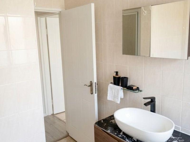 A modern bathroom featuring a dark marble-topped vanity with a vessel sink, wall-mounted mirror cabinet, and neutral tiled finishes.