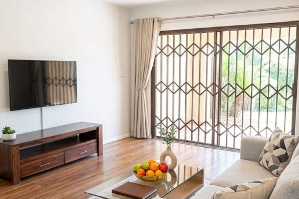 A bright living room featuring laminate flooring, recessed downlighting, and a sliding glass door with a security gate leading to the exterior.