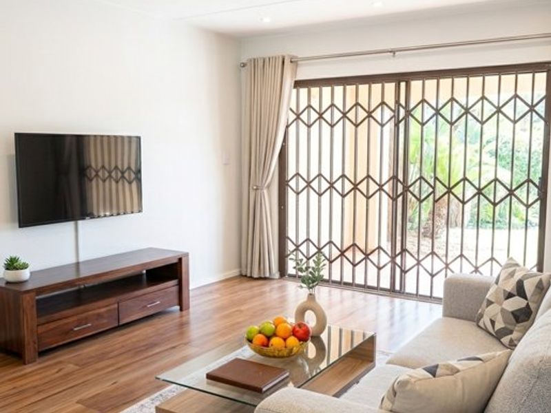 A bright living room featuring laminate flooring, recessed downlighting, and a sliding glass door with a security gate leading to the exterior.