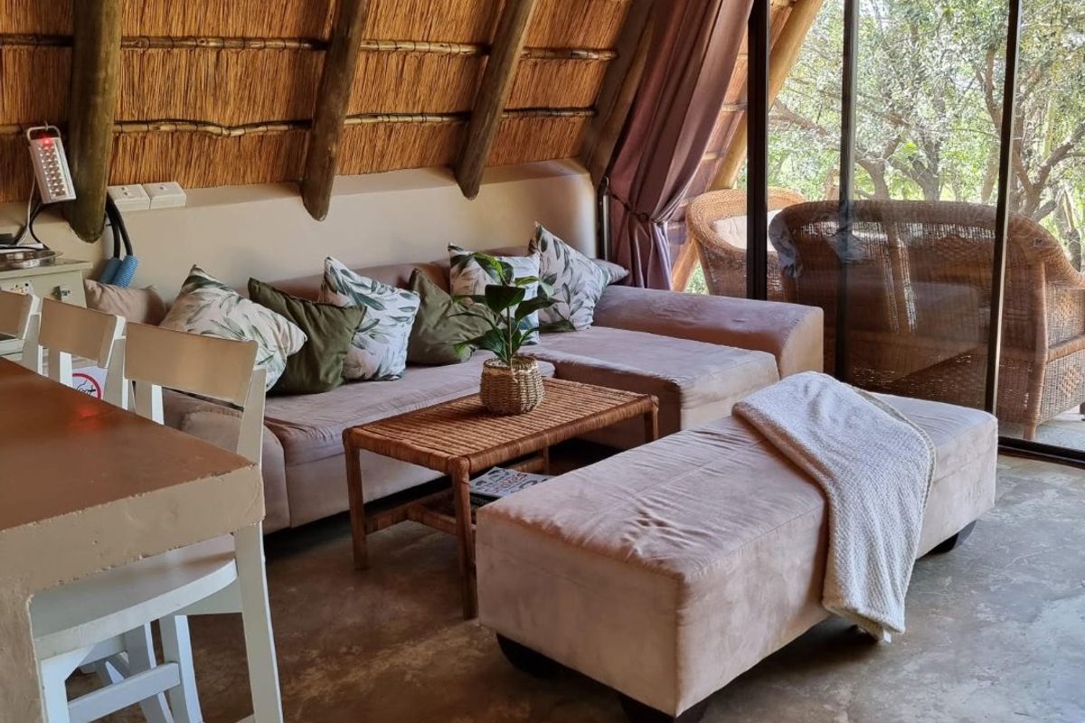 Cozy living area featuring a unique thatched roof with exposed timber rafters, concrete flooring, and large sliding glass doors opening to the outdoors.