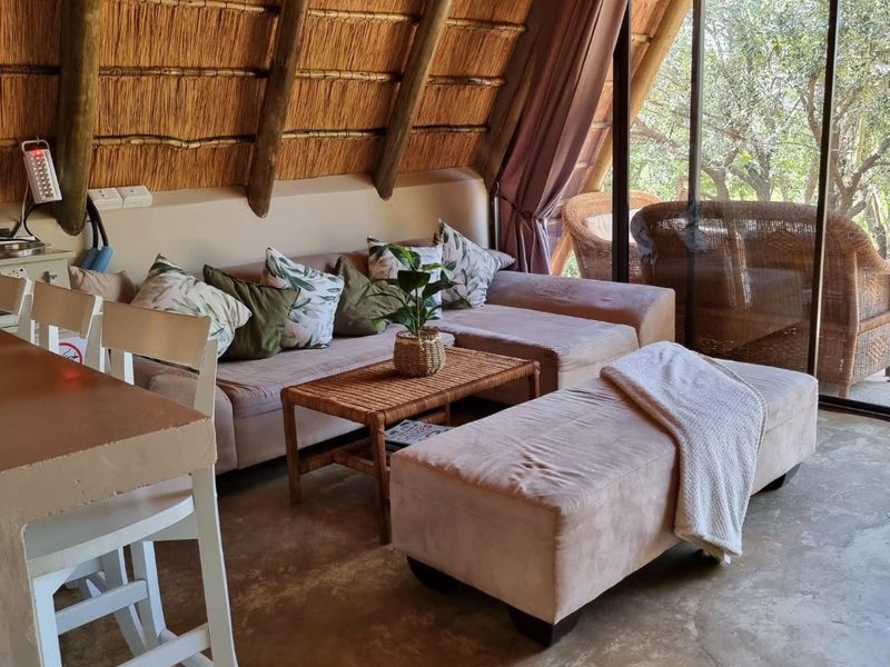 Cozy living area featuring a unique thatched roof with exposed timber rafters, concrete flooring, and large sliding glass doors opening to the outdoors.