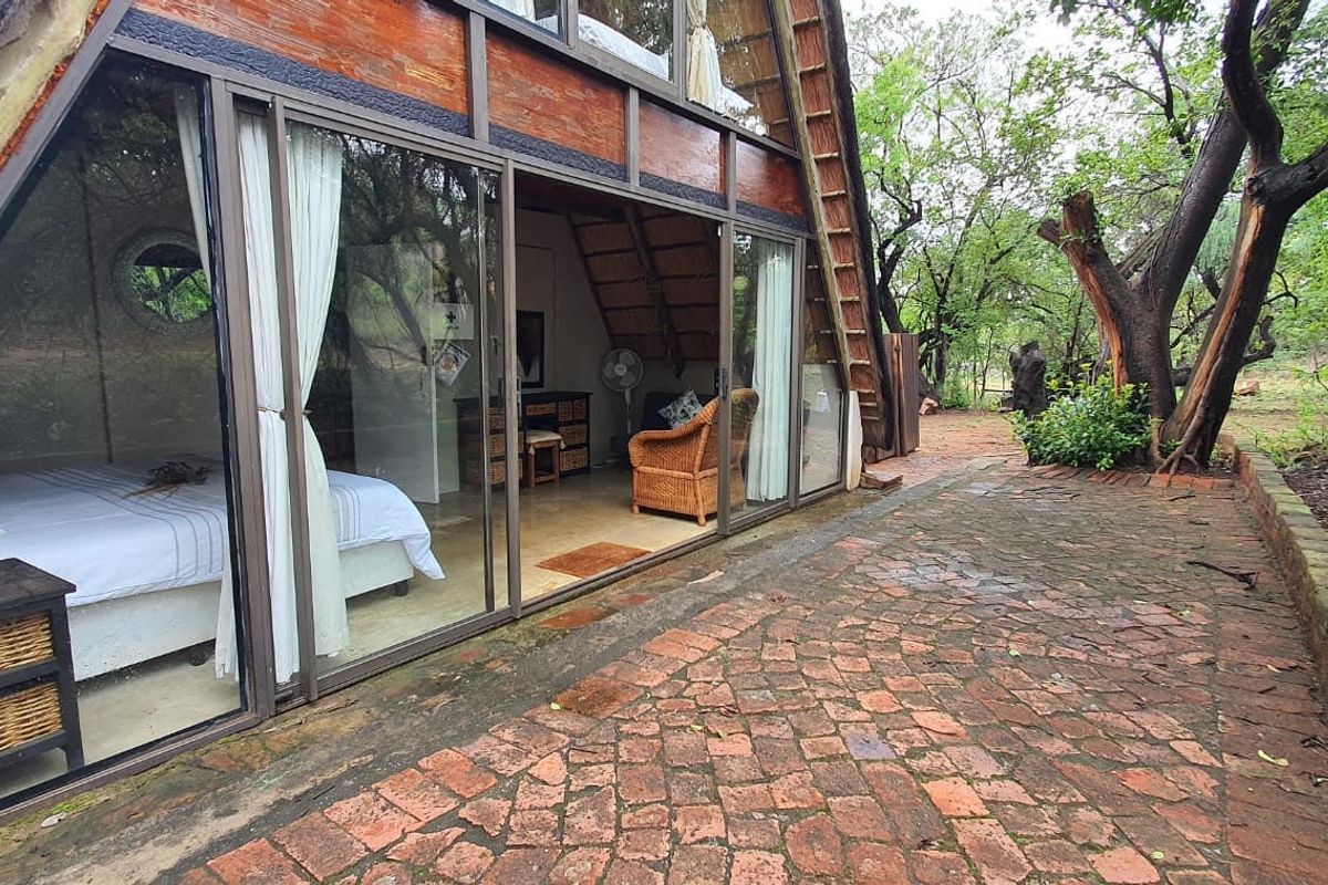 A view of an A-frame house exterior featuring a brick paved patio and large sliding glass doors leading into the bedroom.