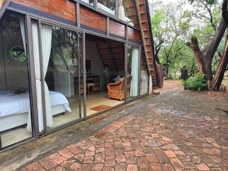 A view of an A-frame house exterior featuring a brick paved patio and large sliding glass doors leading into the bedroom.