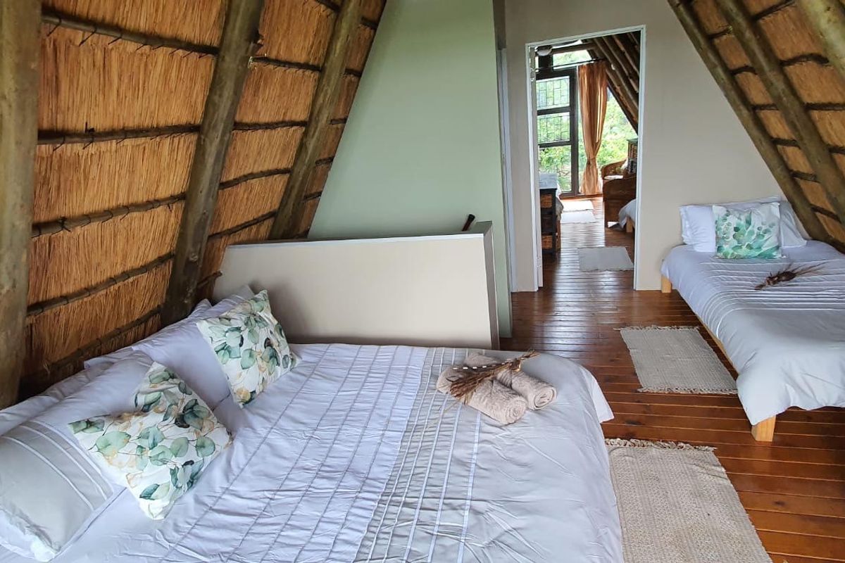 A rustic bedroom featuring a distinctive A-frame design with exposed timber rafters, a thatched roof, and timber flooring.