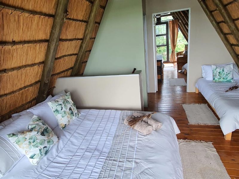 A rustic bedroom featuring a distinctive A-frame design with exposed timber rafters, a thatched roof, and timber flooring.