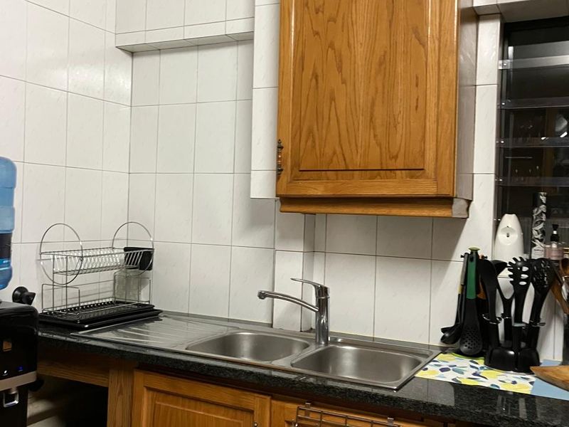 A functional kitchen area featuring wooden cabinetry, granite countertops, and a double bowl stainless steel sink with tiled splashbacks.