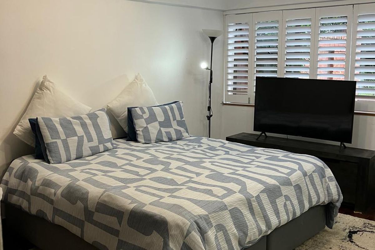 A well-maintained bedroom featuring white plantation shutters, a central ceiling light fixture, and classic picture rail detailing.