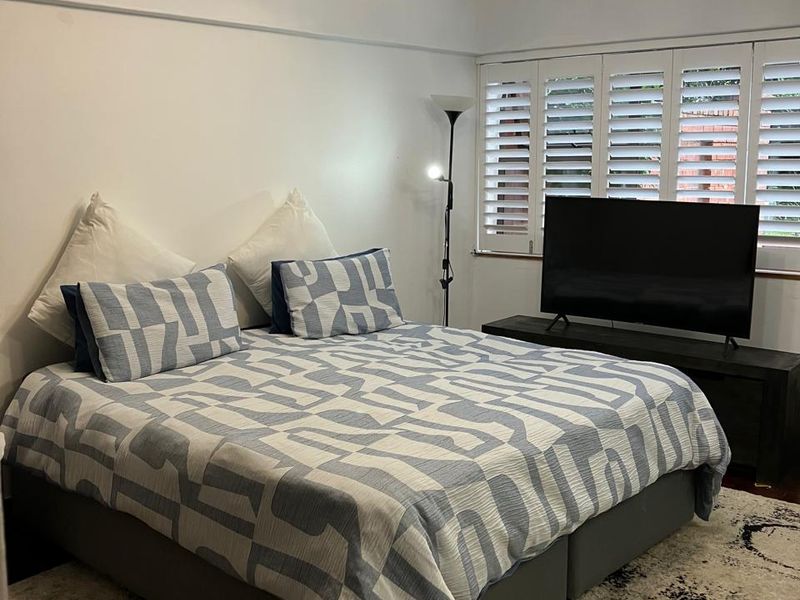 A well-maintained bedroom featuring white plantation shutters, a central ceiling light fixture, and classic picture rail detailing.