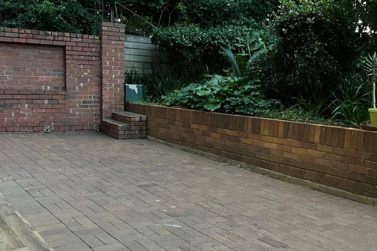 A private rear courtyard featuring brick paving, a raised brick garden bed, and a brick boundary wall with established greenery.