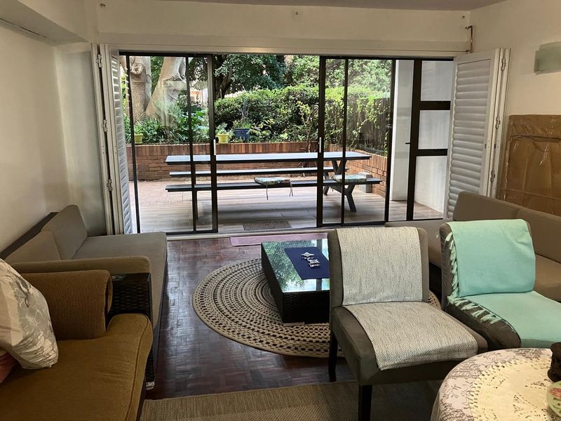 Spacious living area featuring classic parquet flooring and large sliding glass doors that open onto a private paved patio and garden area.
