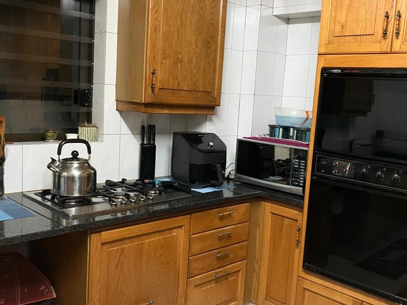 A functional kitchen featuring traditional wooden cabinetry, granite countertops, a built-in oven, and a gas hob with tiled finishes throughout.