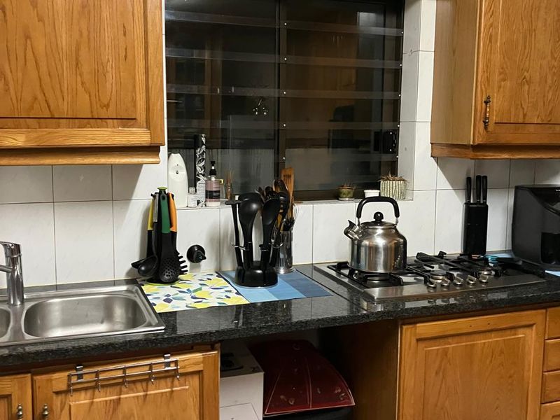 A functional kitchen featuring traditional wooden cabinetry, granite countertops, a gas hob, and a tiled backsplash with a window overlooking the exterior.