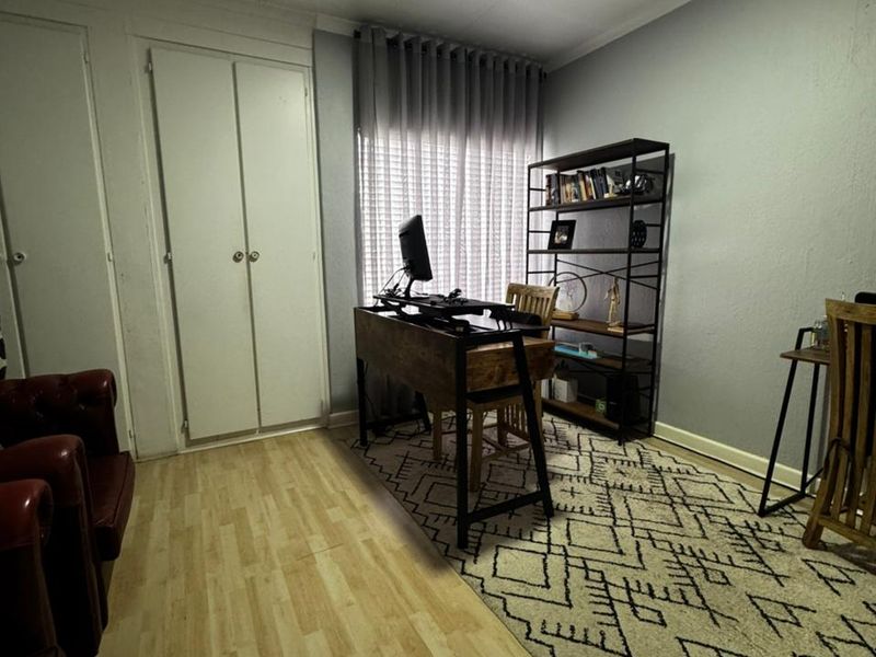A functional home office space featuring laminate flooring, built-in storage cupboards, and neutral wall finishes.