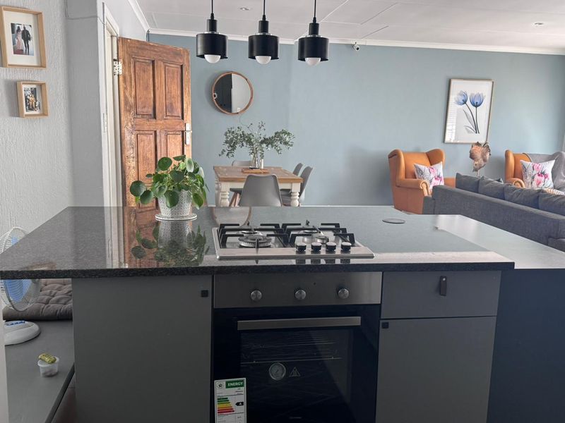 Open plan living area featuring a central kitchen island with a built-in gas cooktop and oven, flowing into a dining and lounge space.