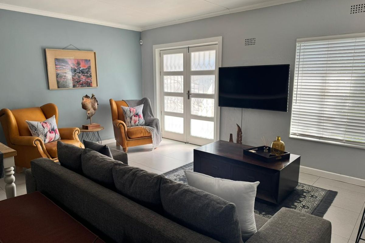 A well-maintained living room featuring tiled floors, neutral wall tones, and double glass doors providing natural light and access to the exterior.