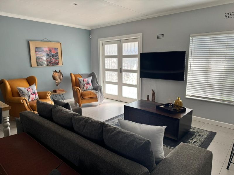 A well-maintained living room featuring tiled floors, neutral wall tones, and double glass doors providing natural light and access to the exterior.