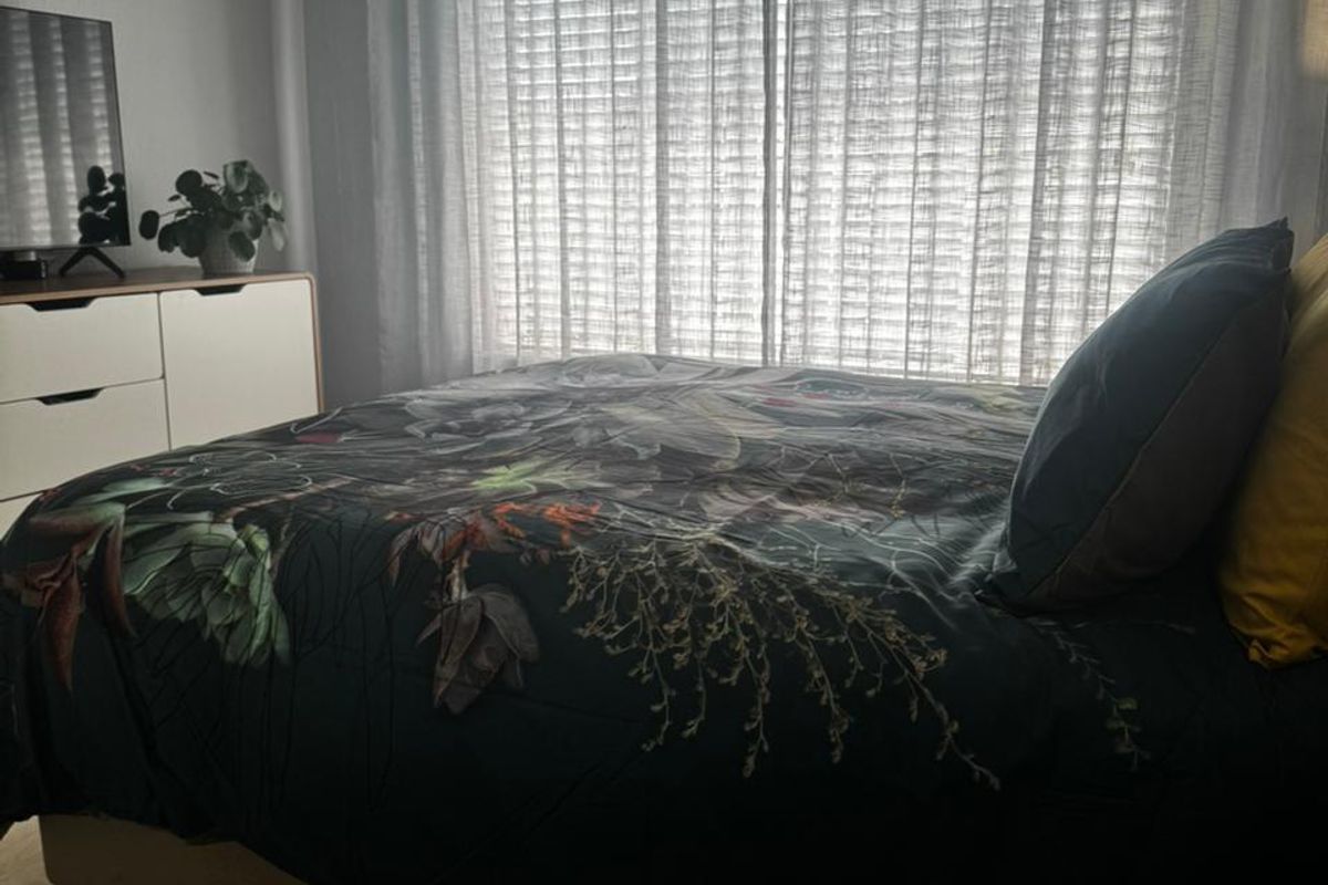 A cozy bedroom featuring light-toned laminate flooring and large windows dressed with sheer curtains, providing natural light to the space.