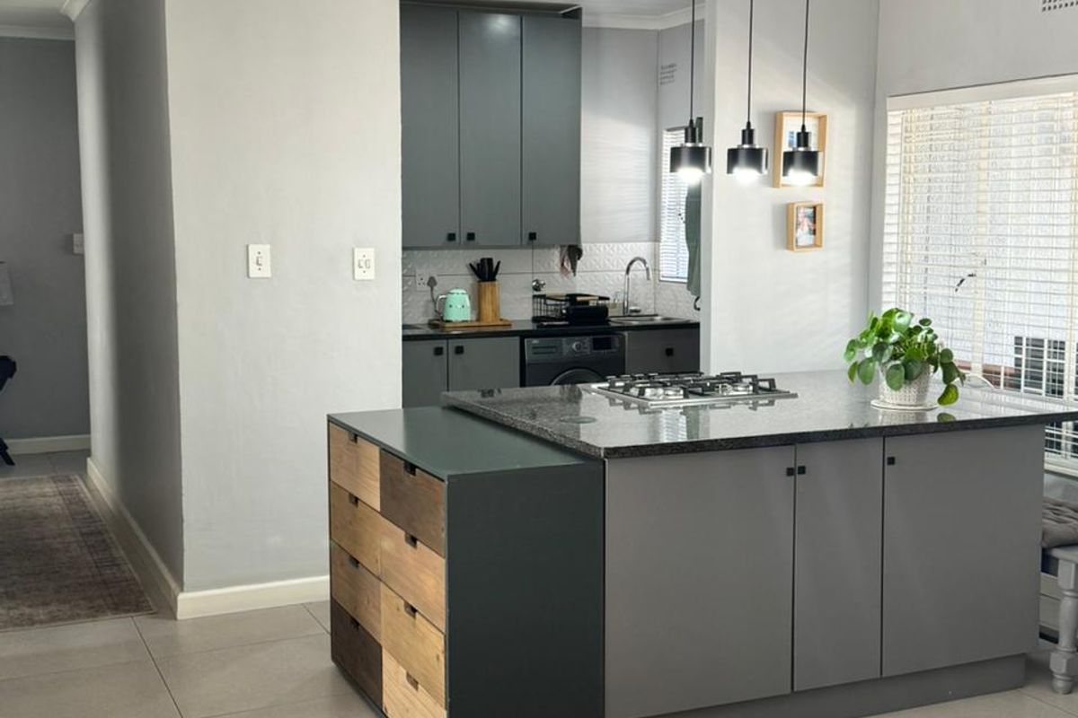 Modern kitchen featuring a central island with a gas cooktop, granite countertops, dark grey cabinetry, and tiled flooring with contemporary pendant lighting.
