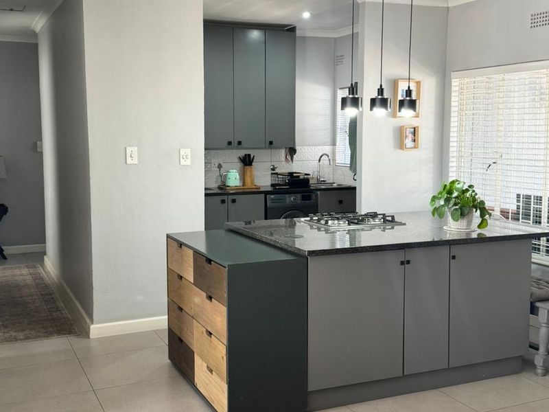 Modern kitchen featuring a central island with a gas cooktop, granite countertops, dark grey cabinetry, and tiled flooring with contemporary pendant lighting.