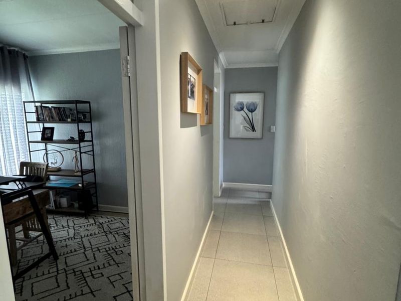 A clean, well-lit hallway featuring neutral tiled flooring and recessed ceiling lights, providing access to adjacent living spaces.