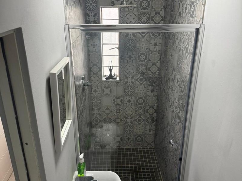 A compact, modern bathroom featuring a glass-enclosed shower with decorative patterned wall tiles, a wall-mounted basin, and mosaic floor tiling.