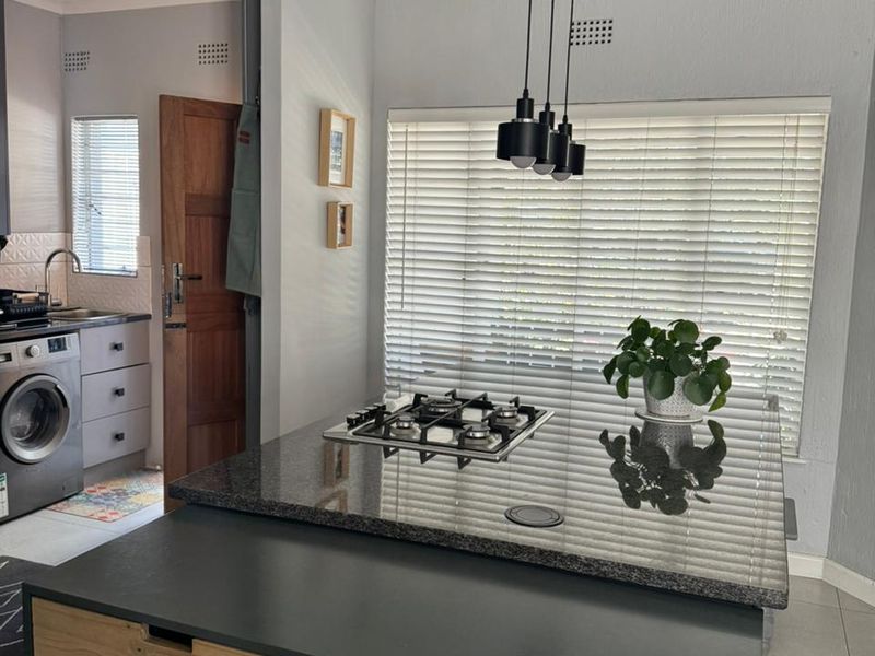 Modern kitchen featuring a central island with a built-in gas hob, granite countertops, stylish pendant lighting, and integrated cabinetry with a separate laundry nook.