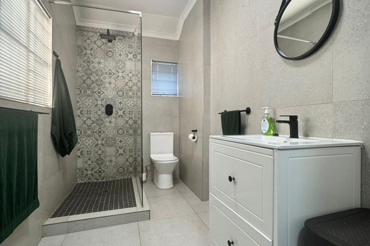 Modern bathroom featuring a walk-in shower with decorative tile accents, a contemporary vanity unit, and neutral floor-to-ceiling wall tiles.