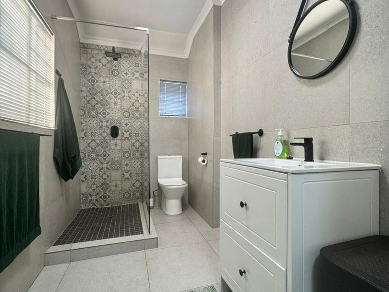 Modern bathroom featuring a walk-in shower with decorative tile accents, a contemporary vanity unit, and neutral floor-to-ceiling wall tiles.