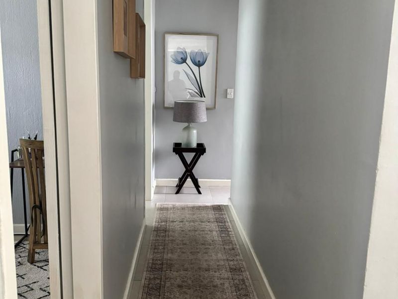 A clean and well-maintained hallway featuring neutral grey walls, coving, and tiled flooring, providing access to adjacent rooms.