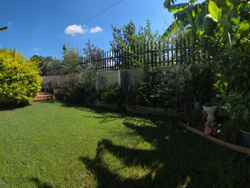A private rear garden featuring a well-maintained lawn, established greenery, and secure perimeter fencing with integrated security spikes.