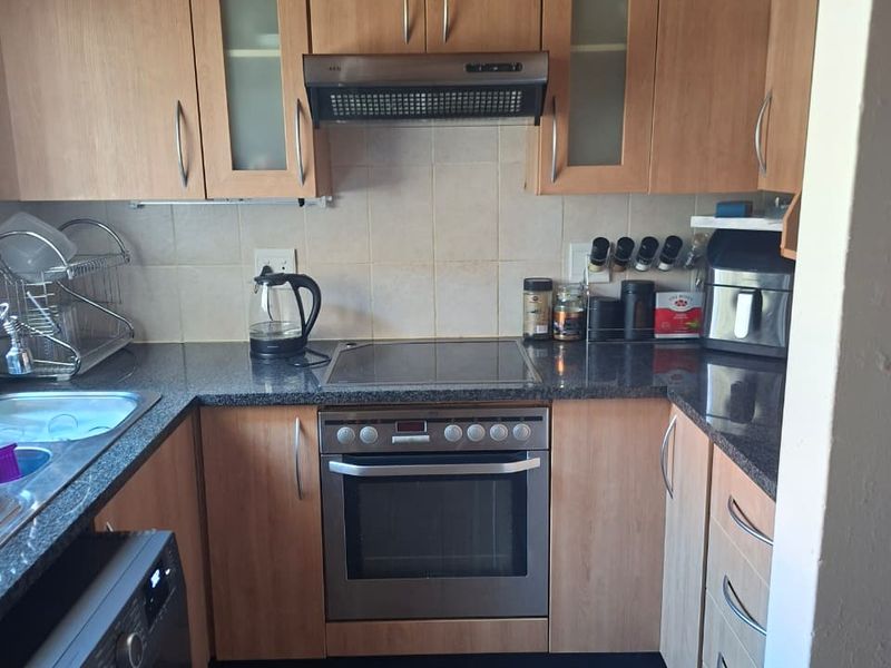 Compact kitchen featuring wood-finish cabinetry, granite countertops, integrated stainless steel oven and hob, and tiled flooring.